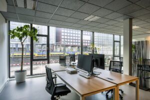 Modern kantoorinterieur aan de De Ruijterkade met uitzicht op het spoor en passerende NS-trein.